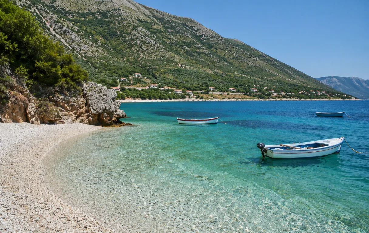 The pebble coves of Radhimë with waterfront houses below the Karaburun hills